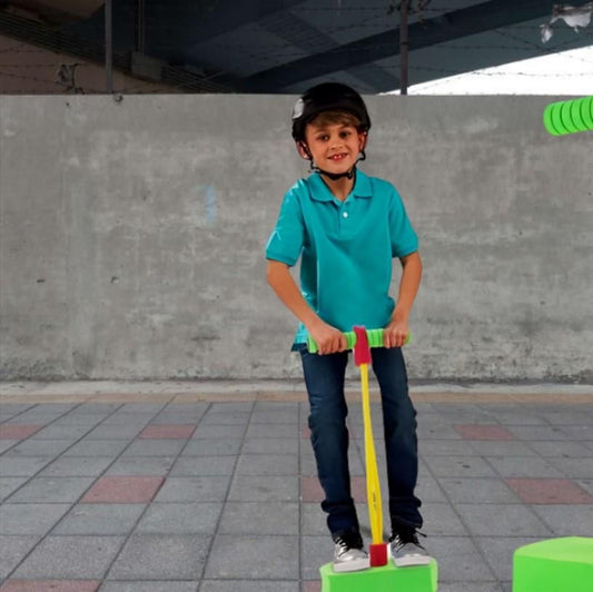 Child in a blue shirt using a foam pogo jumper for kids, smiling with a helmet on